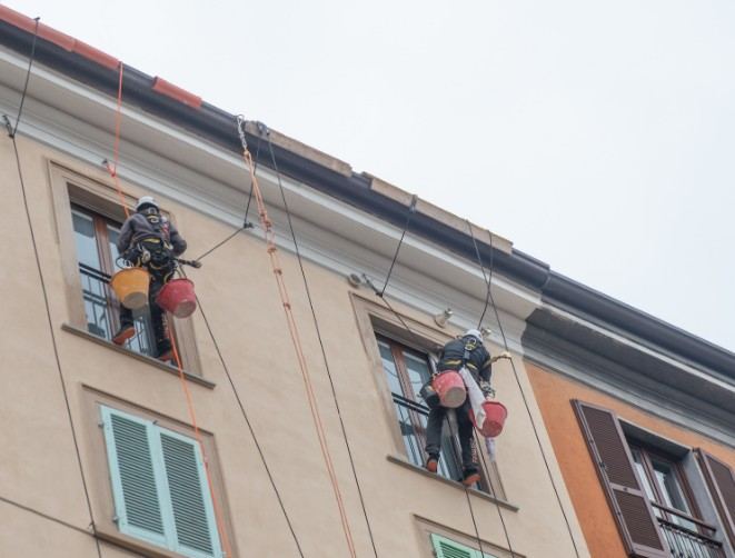 Dos técnicos suspendidos por cuerdas trabajando en la fachada de un edificio de viviendas